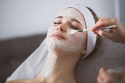 Beautician applying enzymatic peeling on woman's face in spa