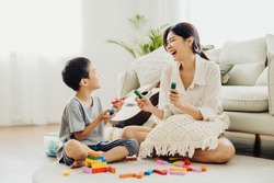 Cute Asian woman and kid playing educational toys together in living room. Mom and son play cubes and laugh Happy family. Young mother and son doing activities together at home.