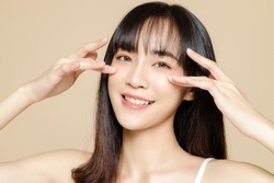 Beautiful young Asian woman with bangs and fresh smooth skin. Cute female model with natural makeup and sparkling eyes on beige background. Face care, Facial treatment, Cosmetology, beauty and spa.