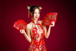 Beautiful Asian woman with clean fresh skin wearing traditional cheongsam dress holding red envelopes or Ang Pao on red background. Happy Chinese new year. Chinese text means great luck great profit.
