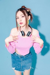 Young fashionable cute carefree Asian woman wearing headphone and roller skate with perfect slim body on isolated blue background. Positive model having fun posing indoors. Cheerful and happy.