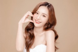 Young Asian beauty woman curly long hair with korean makeup style touch her face and perfect skin on isolated beige background. Facial treatment, Cosmetology, plastic surgery.