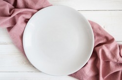 White empty plate on a pink napkin and white wooden table
