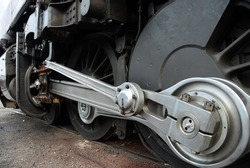 Foreshortened view of a silve metal valve gear assembly main drive rod linkage and drive wheels with on a black steam locomotive
