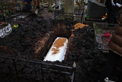 Grieving relatives bury a white coffin in a pit, throwing the coffin to the ground