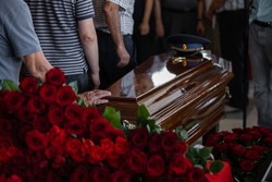 People came to say goodbye to a deceased relative of a military officer in the church before the burial, carrying flowers and touching the wooden brown coffin. on which lies a military cap