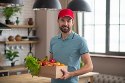 Courrier. Man in a red hat holding the box with groceries on the table