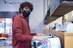 Curly-haired food delivery courrier ina protective mask at work