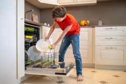 Boy putting dishes into an open dish-washing machine