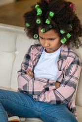 Dark-skinned girl in curlers sitting with hands folded