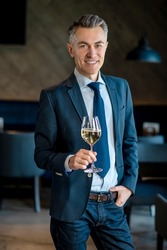 An elegant man in a suit with a glass of wine in hands