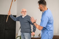 Exasperated pensioner threatening his caretaker with his cane