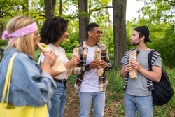 Group of young people in the forest standing near the car and eating sandwiches