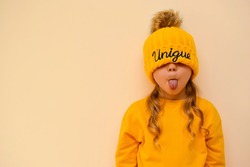 A cute little girl pulls on an orange cap with the words 