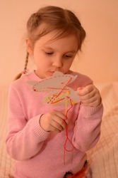 The child learns to embroider with a cross.  A cute little girl with pigtails learns to cross-stitch using a safe plastic needle and a cardboard trainer in the shape of a fox or a kitten.