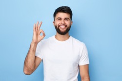 handsome positive bearded man in white T-shirt isolated on blue background showing ok sign.close up portrait, body language, everything is ok, allright. people and success concept. successful business