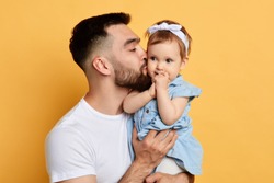 Happy young handsome man holding and kissinga little girl, isolated on yellow. cose up photo. isolated yellow background.tasty yummy daughter