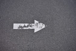 White painted arrow on pavement, weathered and worn white paint. Pointing to the right.