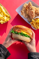 A girl holding a chicken crunchy burger into her hands,a paper dish of crunchy chicken,a paper dish of french fries on a red background.
fresh lettuce,cheese.