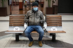 Portrait of man with a medical mask sitting on bench with social distancing symbols in the train station 