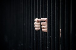 Closeup of hands behind a metallic fence - Captivity concept