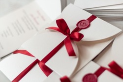 White card invitations sealed with red wax stamp and closed with beautiful ribbon, wedding stationery on the table