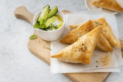 Filo pastry triangle hand pies, stuffed savory crispy bakes served with yogurt tzatziki dip on wooden board