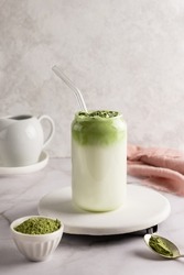 Dalgona matcha latte in glass with matcha powder on white background, whipped grean tea with milk.