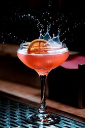 Lemon garnish splashing in pink craft cocktail coupe glass