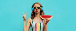 Summer portrait of stylish woman in headphones listening to music blowing her lips sends kiss with fresh juicy slice of watermelon on blue background, blank copy space for advertising text