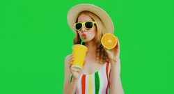Summer portrait of beautiful young woman drinking fresh juice with slice of orange fruit wearing a straw hat, sunglasses on green background