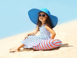 Pretty little girl in a striped dress and hat relaxing on the beach near sea, summer, vacation, travel - concept