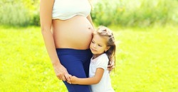 Pregnancy and family concept, happy pregnant woman, little child daughter touches belly mother in summer day