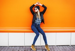 Street fashion concept - stylish cool girl in rock black style posing against a colorful urban wall