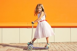 Portrait of active little girl child skating on scooter in the city