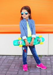 Stylish little girl child with skateboard over orange background