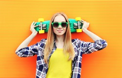 Fashion pretty blonde girl wearing a sunglasses with skateboard having fun over colorful yellow background