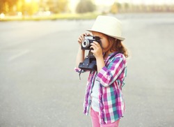 Little girl child with retro camera doing snapshot outdoors, profile view