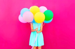 Woman is hides her head an air colorful balloons having fun over pink background
