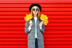 Fashion autumn smiling woman with yellow maple leaves on a red background