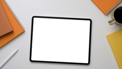 Top up view of trendy workplace with mock up tablet, office supplies and coffee cup on white table background
