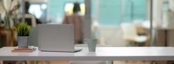 Close up view of comfortable office desk with laptop, mug, tree pot, office supplies and copy space on white table in glass partition office