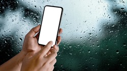 Close up view of male hands using mock-up smartphone in blurred raindrop on glass window background, clipping path