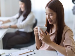 Asian young female employee sipping hot tea at her office desk. Businesswoman relaxed with hot drink before work.
