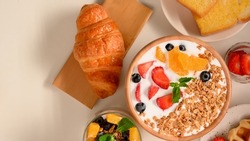 Top view of a yummy healthy breakfast set with homemade granola  yogurt bowl with fresh fruits, baked croissant, toasts and fresh fruit on table.