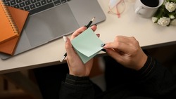 A creative female taking notes on sticky notes or notepad over her modern office workspace. top view