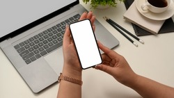 Close-up shot, Female holding a smartphone white screen mockup over her office workspace. top view