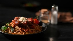 Spaghetti with tomato sauce topped with parmesan cheese in a black plate and black background. food image for luxury restaurant.