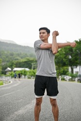 Portrait of a handsome asian young in active and comfy sportswear stretching his arms and body before running, training or jogging.