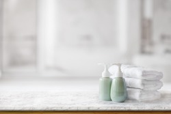 Ceramic soap green bottles and white cotton towels on a marble counter table inside a bright bathroom background.